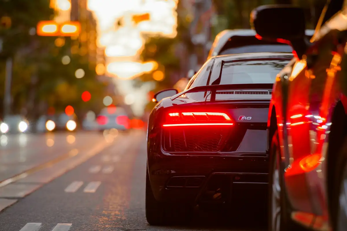 Black sedan pulling away down a wet city street at dusk.