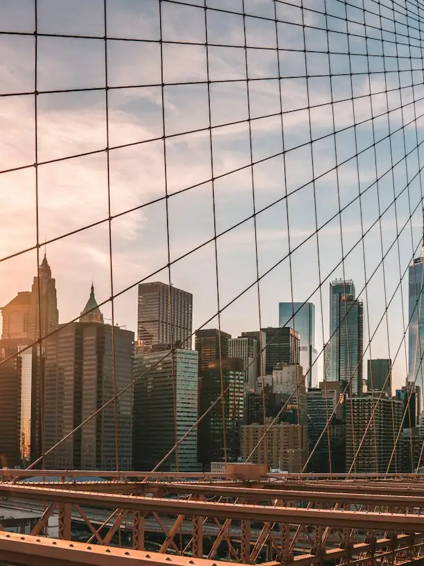 Brooklyn Bridge cables with the skyline behind at sunset.